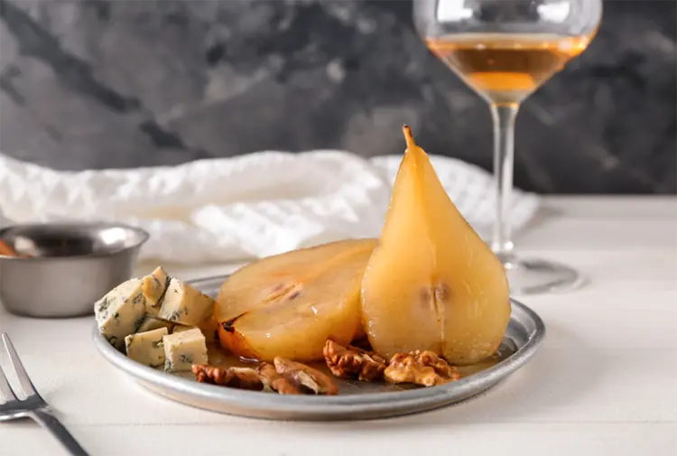 A pear cut in half with a glass of wine, cheese, and nuts.