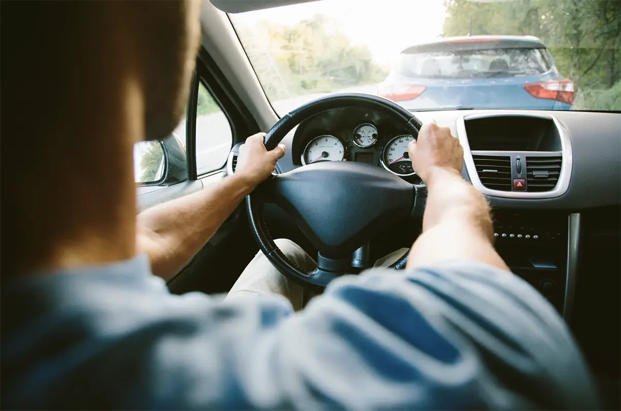 Person driving a car with over the shoulder camera angle.